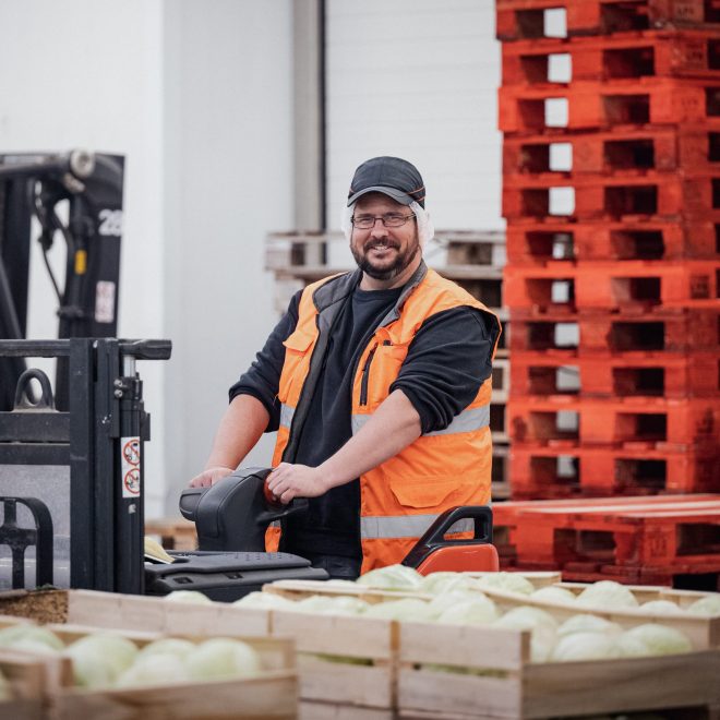 Collaborateur de Priméale, branche Légumes d'Agrial, portant un gilet de sécurité orange et roulant sur un transpalette électrique. Il se trouve derrière des caisses de melons. Collaborateur de Priméale, branche Légumes d'Agrial, portant un gilet de sécurité orange et roulant sur un transpalette électrique. Il se trouve derrière des caisses de melons.
